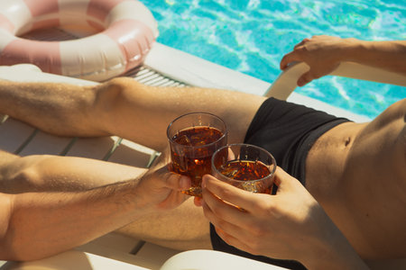 Two man in swimwear clicking glasses of iced drink by poolsideの写真素材