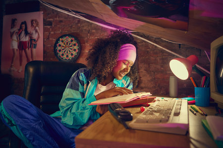 Smiling teen girl writing in notebook under desk lamp in retro room
