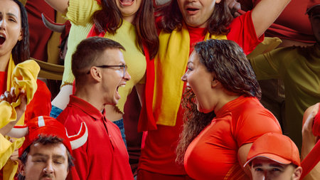 Two sports fans in red and yellow shirts shouting face to face during match.