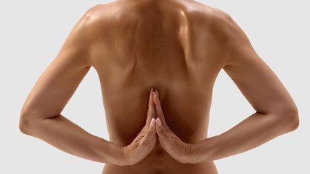 Bare back with arms in reverse prayer pose on light background