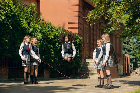 Schoolgirls jumping rope outside campus building with laughter and excitementの写真素材