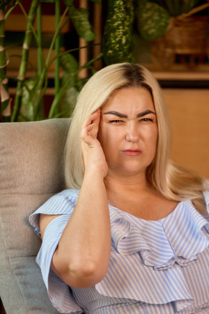 Blonde woman touching temple with pained face indoors