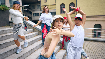 Female dancer in cap leading group with strong emotional expression on city stairs