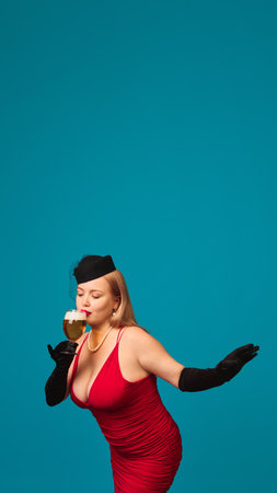 Woman in red dress with hat and gloves drinking beer with pose on blue backgroundの写真素材