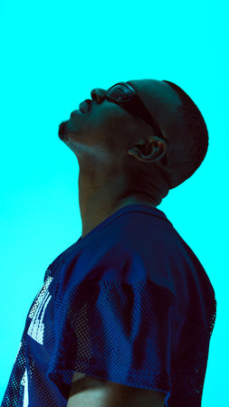 Man in futuristic sunglasses looking upward against bright cyan backgroundの写真素材