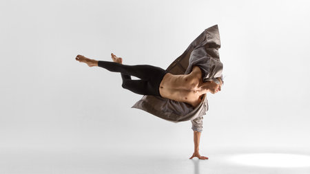 Male dancer balancing on one arm in coat with extended legs and emotional strength