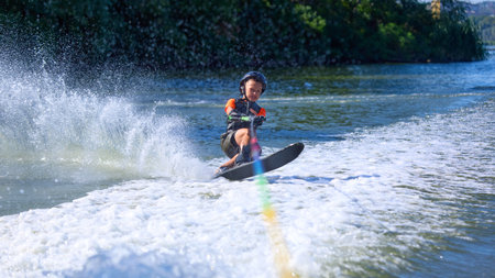 Boy in black helmet leaning forward while water skiing with splash trail