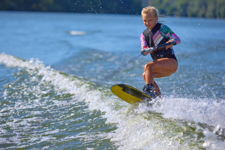 Smiling girl wakeboarder enjoying jump over lake wavesの写真素材
