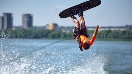 Boy wakeboarder upside down flip stunt on river in bright orange shirtの写真素材