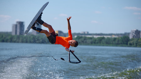 Young wakeboarder mid fall stunt with one hand release above waterの写真素材