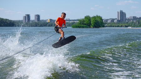 Boy wakeboarder airborne trick over river waves with confident focusの写真素材
