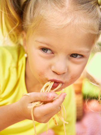 Close up of girl eating spaghetti with messy face at picnicの写真素材