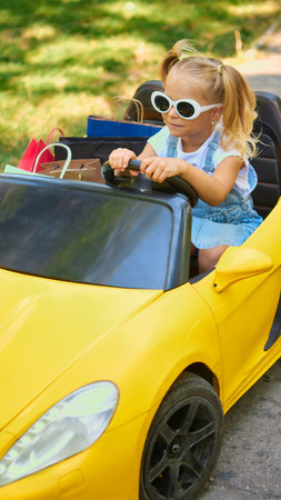 Girl in sunglasses driving toy yellow car with shopping bagsの写真素材