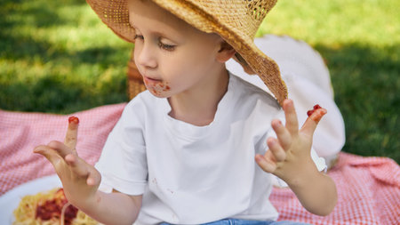 Boy with spaghetti sauce on face and fingers at picnicの写真素材