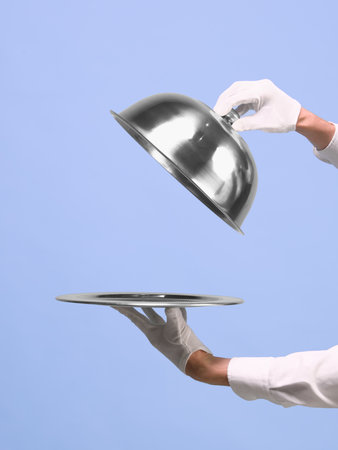 Hands lifting silver cloche from tray on blue background. Negative space for ads
