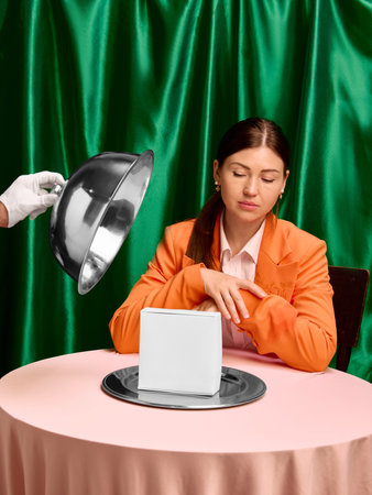 Woman in orange blazer at table with white box on silver plate