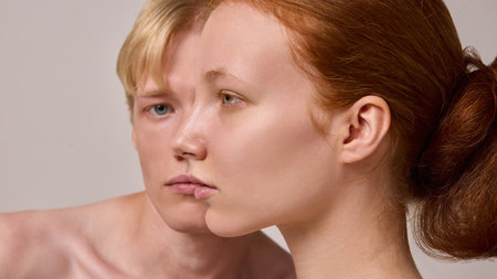Close side profile of red-haired woman with blond man blurred behind on neutral backgroundの写真素材