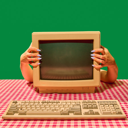 Hands holding vintage computer monitor with keyboard on table.の写真素材