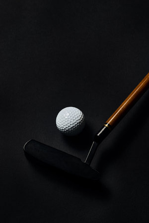 Golf ball and putter with wooden shaft on dark textured surface