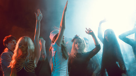 Girls in Halloween costumes dancing with raised hands in smoky neon club atmosphere