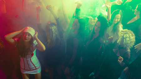 Girls in a crowd in Halloween costumes dancing with bright green neon lightsの写真素材