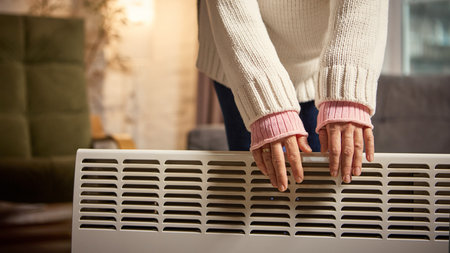 Woman standing by heater warming hands in cozy modern apartmentの写真素材