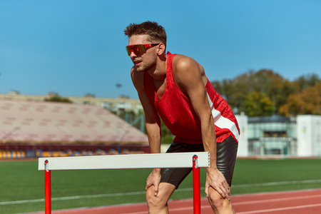 Athlete resting on hurdle after intense training session on sunny trackの写真素材