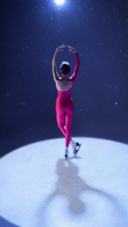 Woman figure skater in pink costume raising arms to light in elegant ballet-inspired positionの写真素材