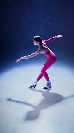 Female skater in pink bodysuit leaning forward in dynamic motion on ice under blue lightの写真素材