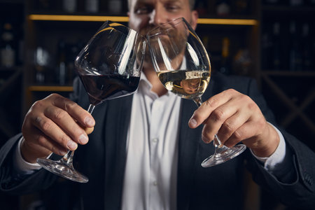 Close up of sommelier toasting with red and white wine in dimly lit barの写真素材