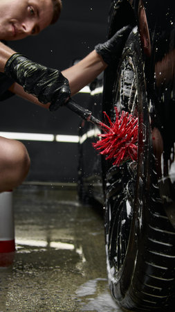Focused worker cleaning wheel rim with red brush at car detailing centerの写真素材