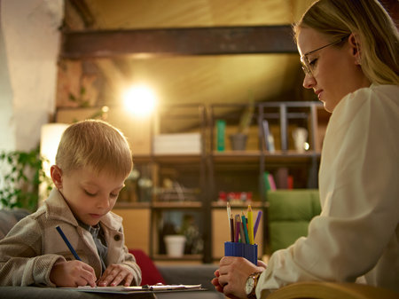 Child drawing with pencil during therapy session while psychologist observes attentivelyの写真素材