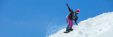Snowboarder in bright retro suit balancing on snowy slope under vivid blue sky. Banner