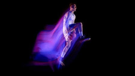 Basketball player in midair holding ball with vivid neon light trail on dark backgroundの写真素材