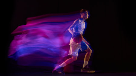 Basketball player dribbling ball in blue and purple motion light on dark backgroundの写真素材