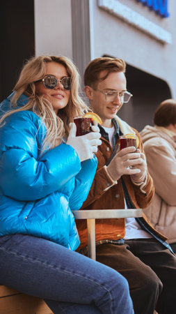 Stylish couple holding mulled wine on winter street terraceの写真素材