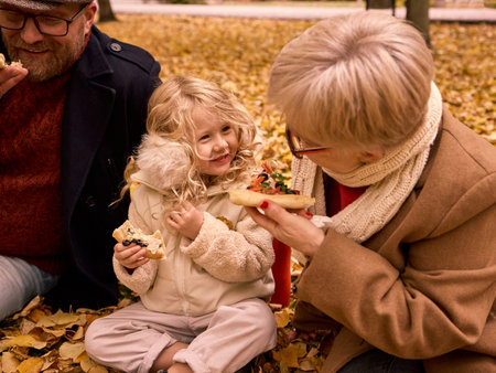 Family eating pizza together on autumn leaves smiling warmlyの写真素材