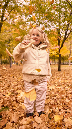 Little girl standing among falling leaves holding hotdog and smilingの写真素材