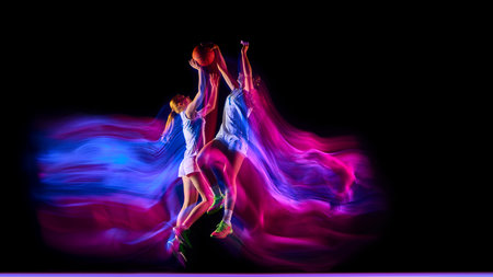 Two basketball players jumping under colorful neon lights in action.
