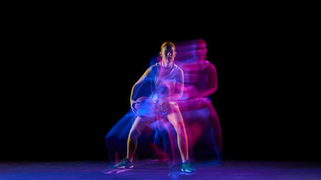 Female basketball player controlling ball under neon motion lights.の写真素材