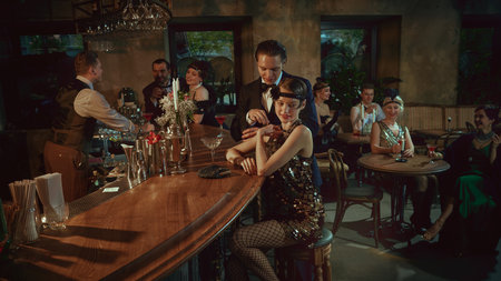 Laughing guests in vintage fashion enjoying cocktails and social moments at the bar