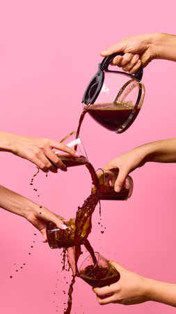 Hands pouring coffee between several glasses in chaotic splash on pink backgroundの写真素材