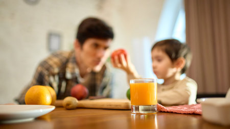 Fresh orange juice in glass with warm father and son morning atmosphere and joyful moodの写真素材