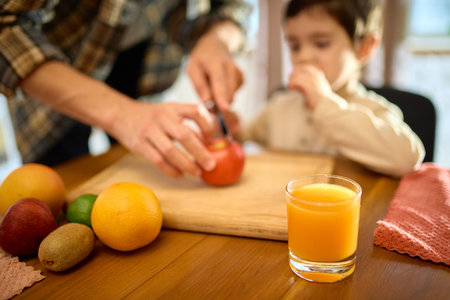 Fresh orange juice in glass with sunny kitchen mood and gentle father and son presenceの写真素材