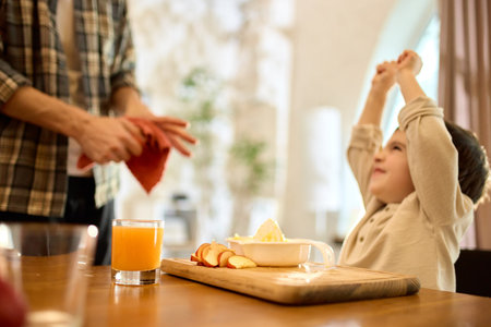 Orange juice in glass with happy son celebrating fresh citrus squeezing in warm kitchenの写真素材