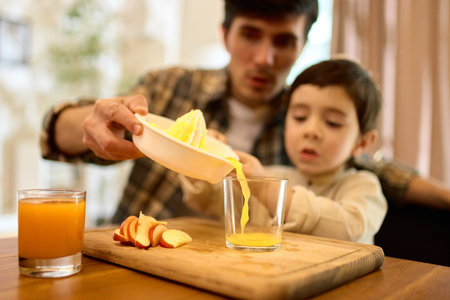 Fresh squeezed citrus juice poured by father and son into glass with warm kitchen moodの写真素材