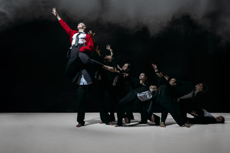 Striking group formation with raised gestures around elevated figure in red jacket creating bold promotional imageryの写真素材