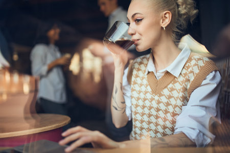 Woman sipping coffee while working with colleagues talking nearbyの写真素材