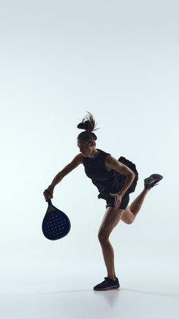 Female padel player jumps for overhead shot in studio on white backgroundの写真素材
