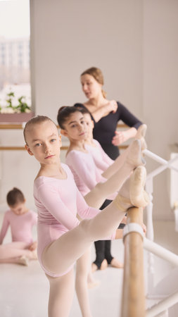 Young ballerina stretching leg at barre during ballet training session.の写真素材